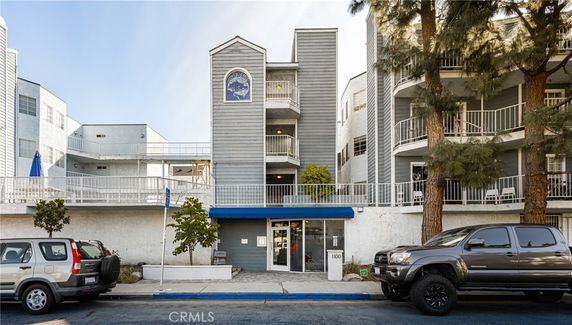 Front view of a multi-story building with balconies and a blue awning entrance.