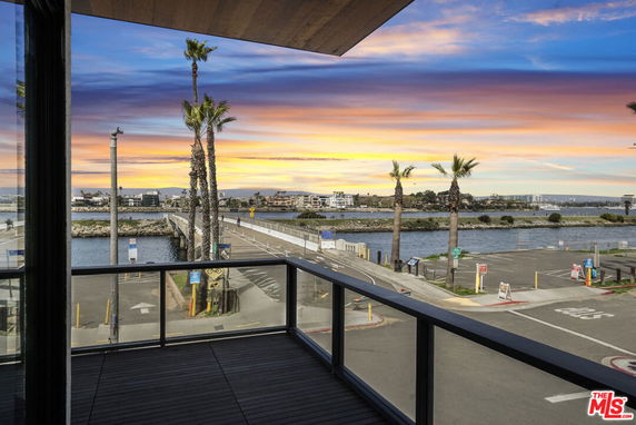 Wide angle view from a building overlooking a waterfront and distant buildings under a colorful sky.