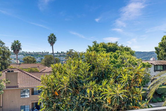 View of houses with red tile roofs and lush greenery, overlooking distant hills.
