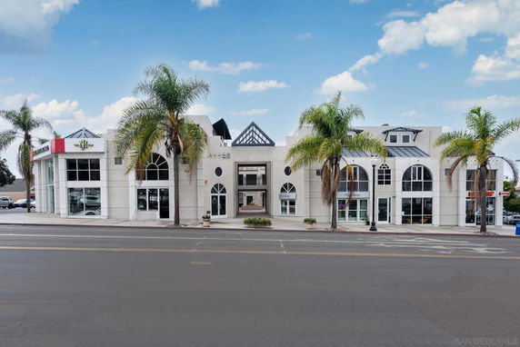 Front view of a modern two-story commercial building with large arched windows and palm trees.