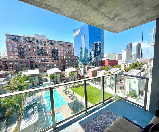 Panoramic view from a building balcony showing a swimming pool, green area, and surrounding cityscape with modern buildings.