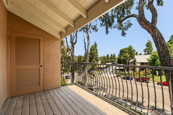 View from a balcony overlooking a street with trees and houses.