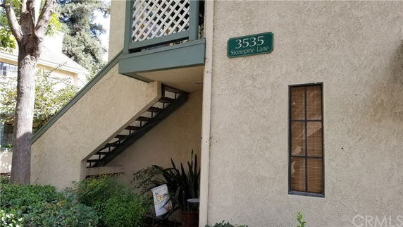 Exterior view of a building entrance with stairs leading to the upper level and a green sign displaying the address.