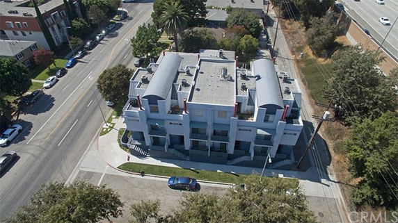 Aerial view of a multi-story building on a street corner with several vehicles and trees nearby.