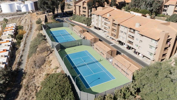Aerial view of apartment buildings with adjacent fenced tennis courts.
