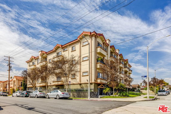 Front view of a multi-story residential building with balconies and parked cars on the street.