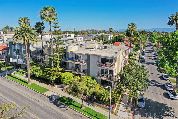 Front view of a multi-story building with balconies and surrounding palm trees.