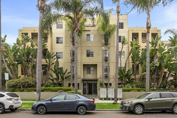 Front view of a multi-story residential building with balconies and surrounded by palm trees.