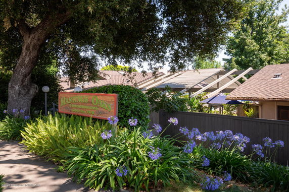 Front view of a residential building with a wooden sign and lush greenery.