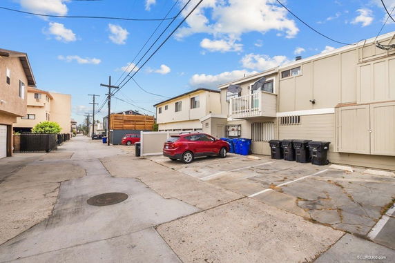 Outdoor parking area behind a building with several parked cars and trash bins, situated in a residential neighborhood.