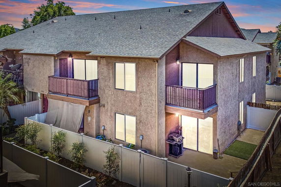 Front view of a two-story house with balconies and a fenced yard.