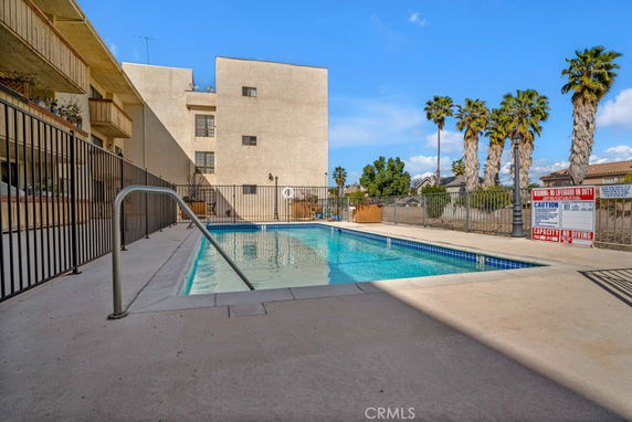 Outdoor swimming pool area with safety fencing and nearby buildings.