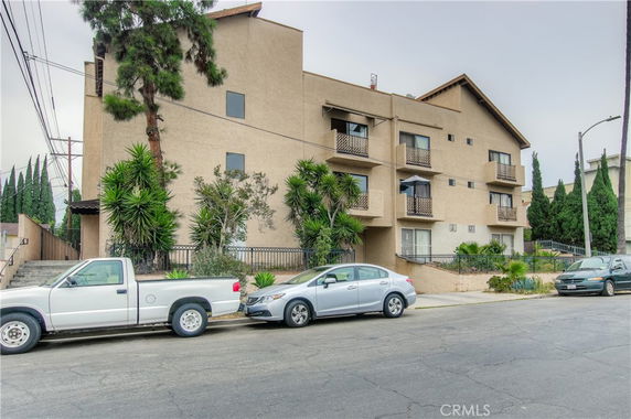 Front view of a multi-story apartment building with balconies and surrounding foliage.