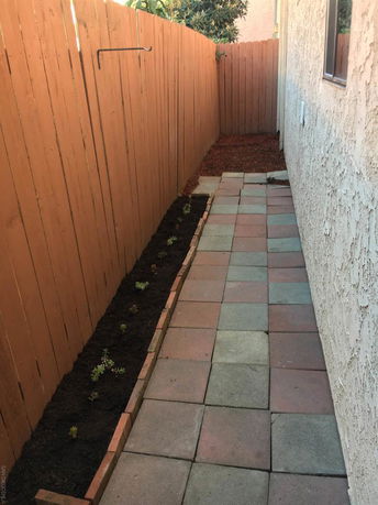 Paved pathway alongside a house with a wooden fence on one side.