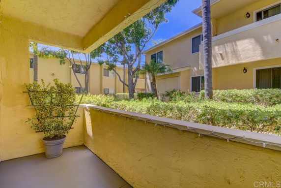 View from a balcony of a yellow residential building overlooking other buildings and greenery.
