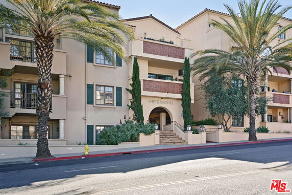 Front view of a multi-story residential building with balconies and palm trees.