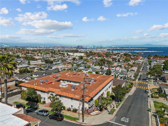 Panoramic view of a coastal residential area with houses and a large building, overlooking the ocean and docks in the distance.