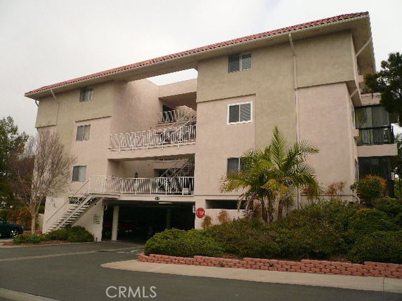 Front view of a multi-story apartment building with visible parking area on the ground floor.