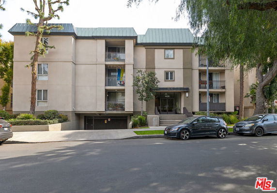 Front view of a multi-story residential building with a parking area in front.