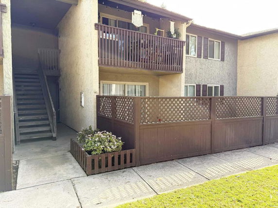 Front view of a two-story building with a balcony and fenced patio area.