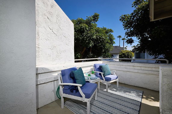 A small rooftop area with two cushioned chairs and a table, enclosed by white walls.