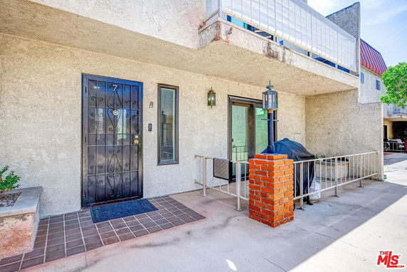 Front view of a building with a metal door and glass sliding door, featuring a small fenced patio area.