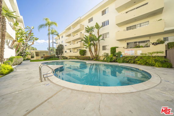 Outdoor swimming pool area adjacent to a multi-story residential building.