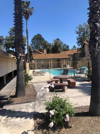 Outdoor view of a swimming pool surrounded by a fence with a nearby covered seating area in a residential complex.