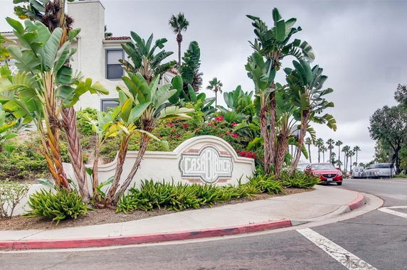 Front view of a building entrance with tropical landscaping and a sign.