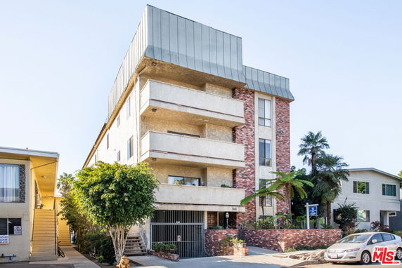 Front view of a multi-story apartment building with balconies and a combination of brick and stucco exterior.