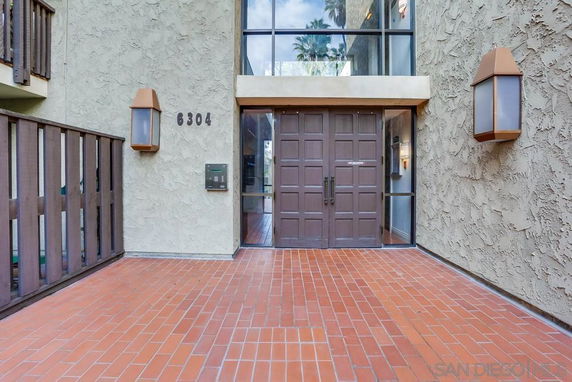 Front view of a building entrance with double wooden doors and brick flooring.