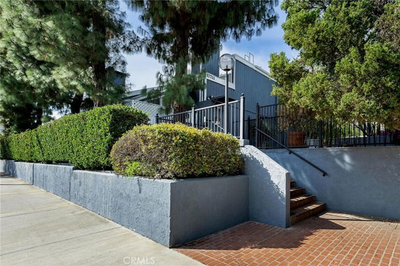 Front view of a house with steps leading up and a fenced entryway surrounded by greenery.