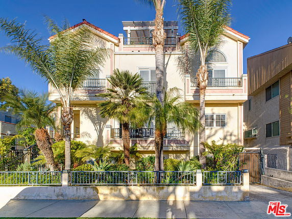 Front view of a multi-story building with balconies and palm trees.