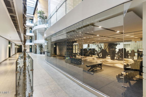 Interior hallway with large glass walls revealing a gym area filled with exercise equipment.