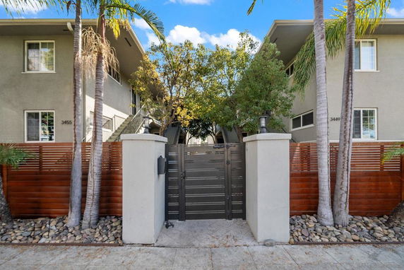 Front view of a two-story residential building with a central gate and surrounding trees.