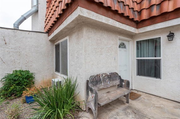Front view of a house with a white door and windows, featuring a decorative bench and plants in the outdoor area.