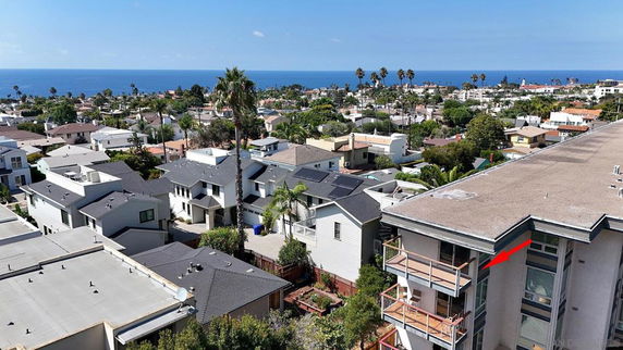 Panoramic view of coastal residential area with rooftops and ocean in the background.