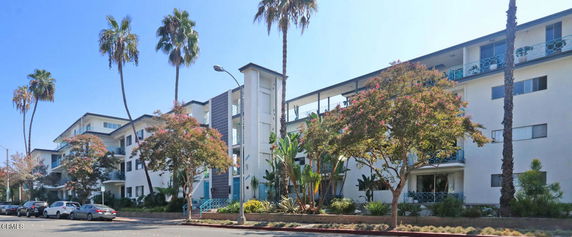 Front view of a multi-story residential building with balconies and palm trees.