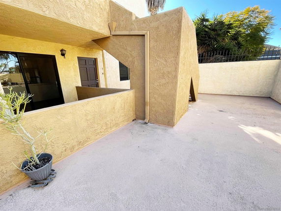 Front view of a building with beige stucco walls and a door, featuring outdoor stairs and a small potted plant.