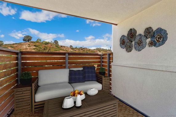 Outdoor seating area with a wooden fence overlooking hills and a blue sky.