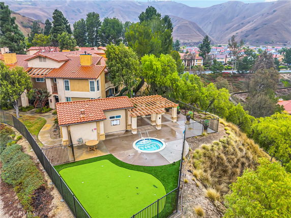 Aerial view of a multi-story house with terracotta roof, overlooking a valley and other houses, with a fenced patio and a small lawn area.