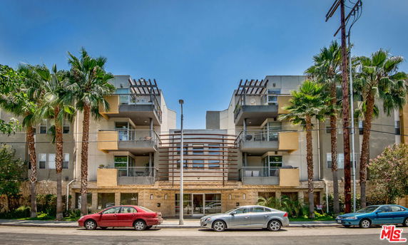 Front view of a multi-story residential building with balconies and palm trees.