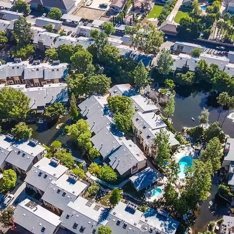 Aerial view of residential area with multiple buildings, trees, and a swimming pool.