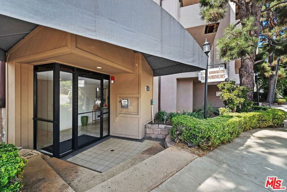 Entrance area of a condominium building with glass doors and an overhang.