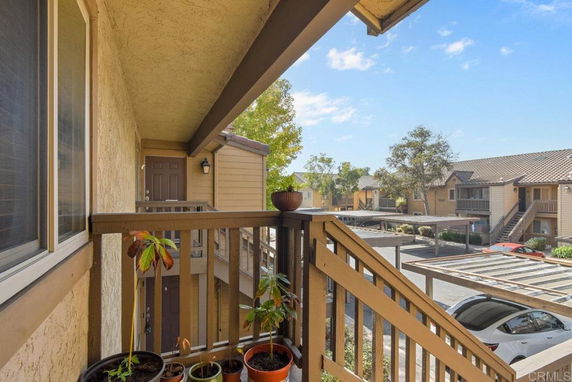 View from a residential balcony overlooking a parking area and neighboring buildings.
