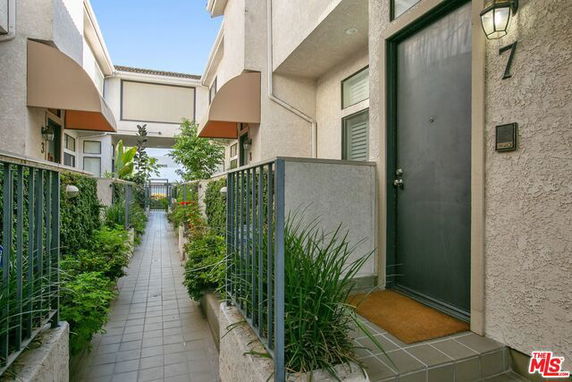 Front view of a multi-story building entrance with plants along a tiled pathway.