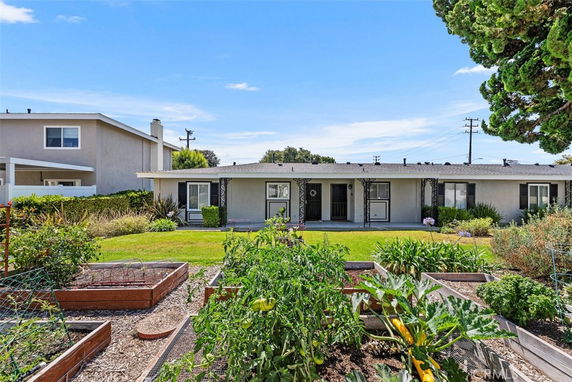 Front view of a single-story house with a porch and garden beds in the foreground.