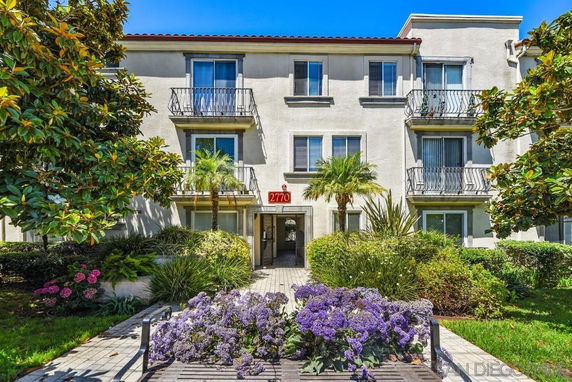 Front view of a three-story residential building with balconies and landscaping.