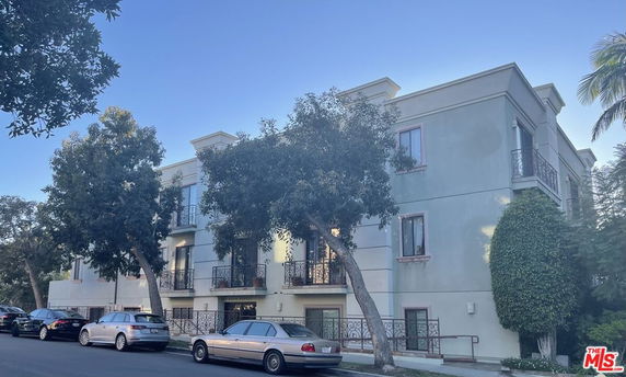 Front view of a three-story residential building with balconies and adjacent trees.
