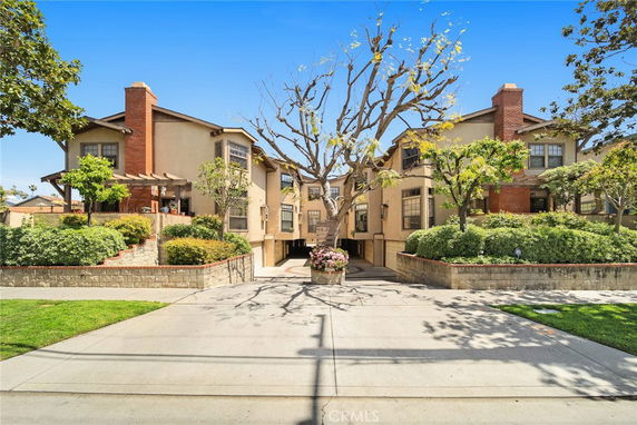 Front view of a multi-story residential building with brick chimneys and landscaped entrance.